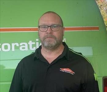 Male employee with beard, standing in front of a green background.